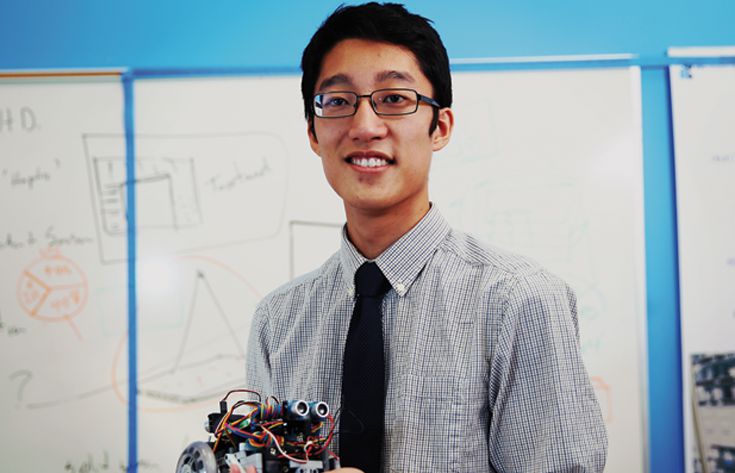 Male student with robot in Hand in front of Whiteboard
